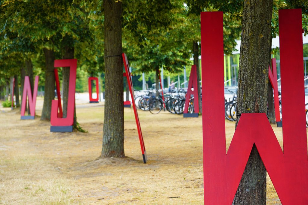 26 Buchstaben-Skulpturen sind auf der Wiese zwischen Hauptgebäude und Gebäude X aufgestellt. Jeder Buchstabe steht für ein anderes Forschungsprojekt der BGHS. Foto: Universität Bielefeld